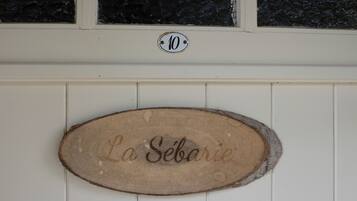 Un letrero de madera con el nombre "La Sébarie" grabado, montado en una pared blanca sobre un ventanal con un marco negro con textura.