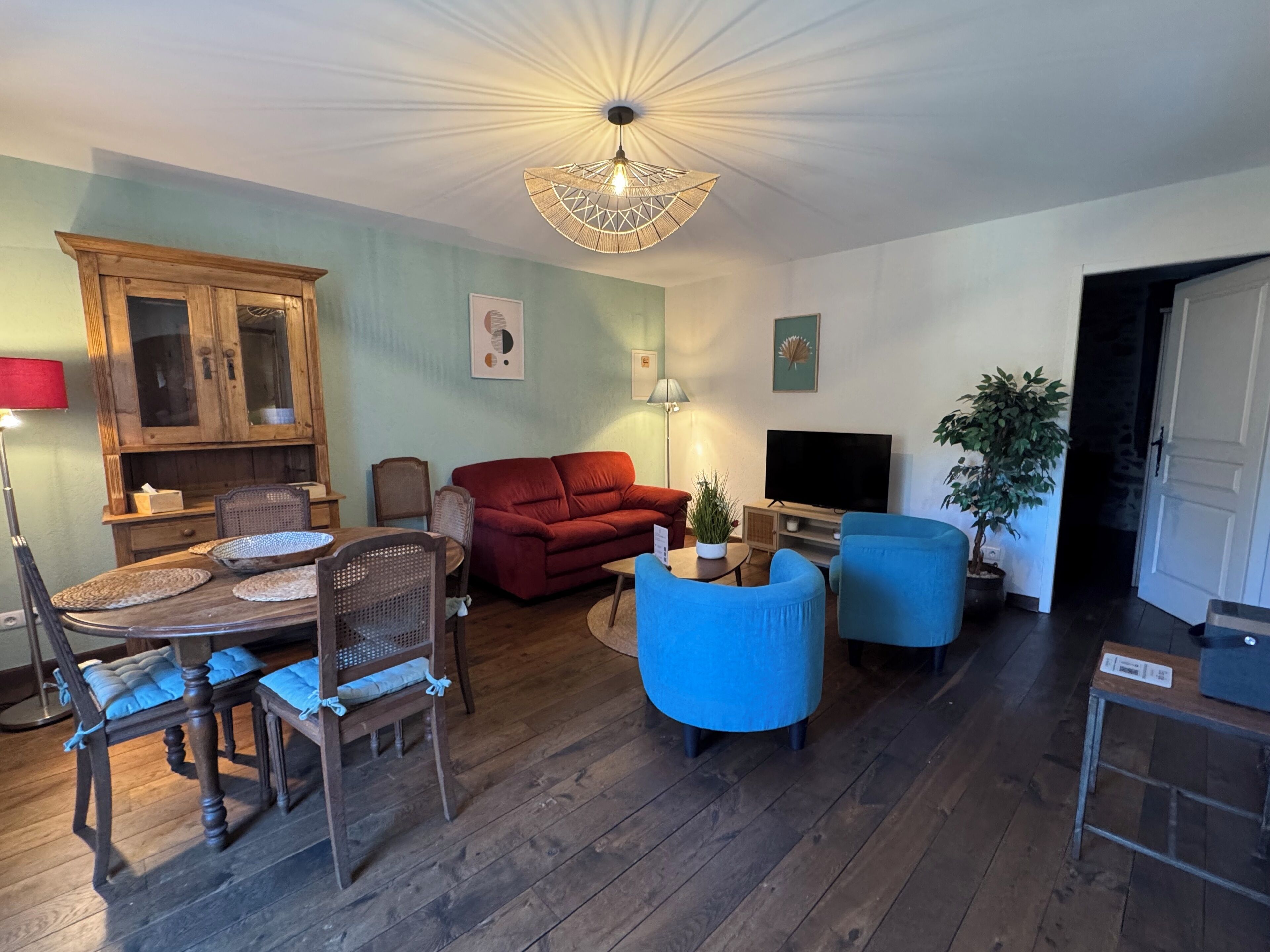 Una sala de estar con una mesa de comedor de madera, un sofá rojo, un sillón azul y un televisor.