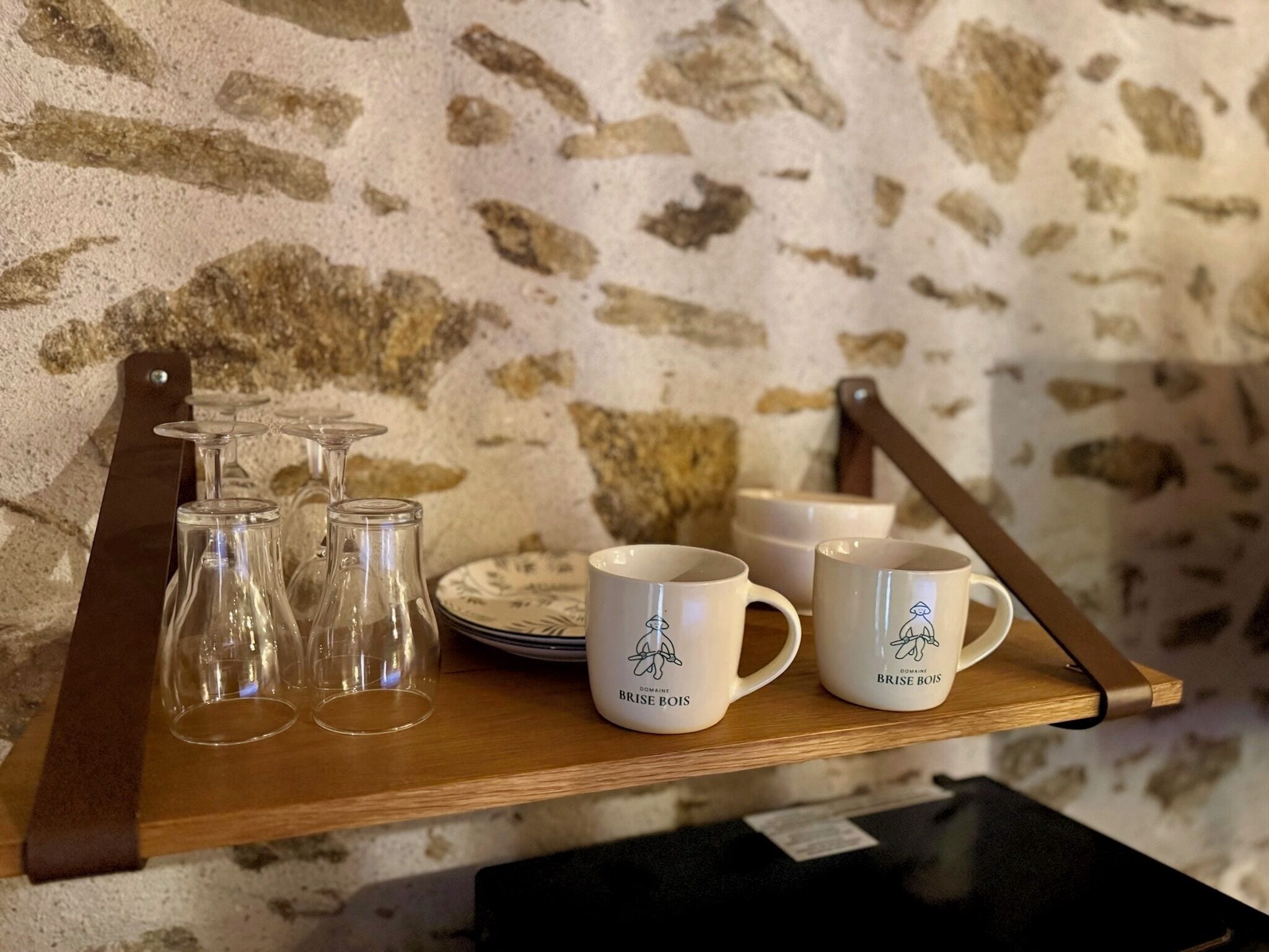 A wooden tray with wine glasses, plates, and branded mugs.