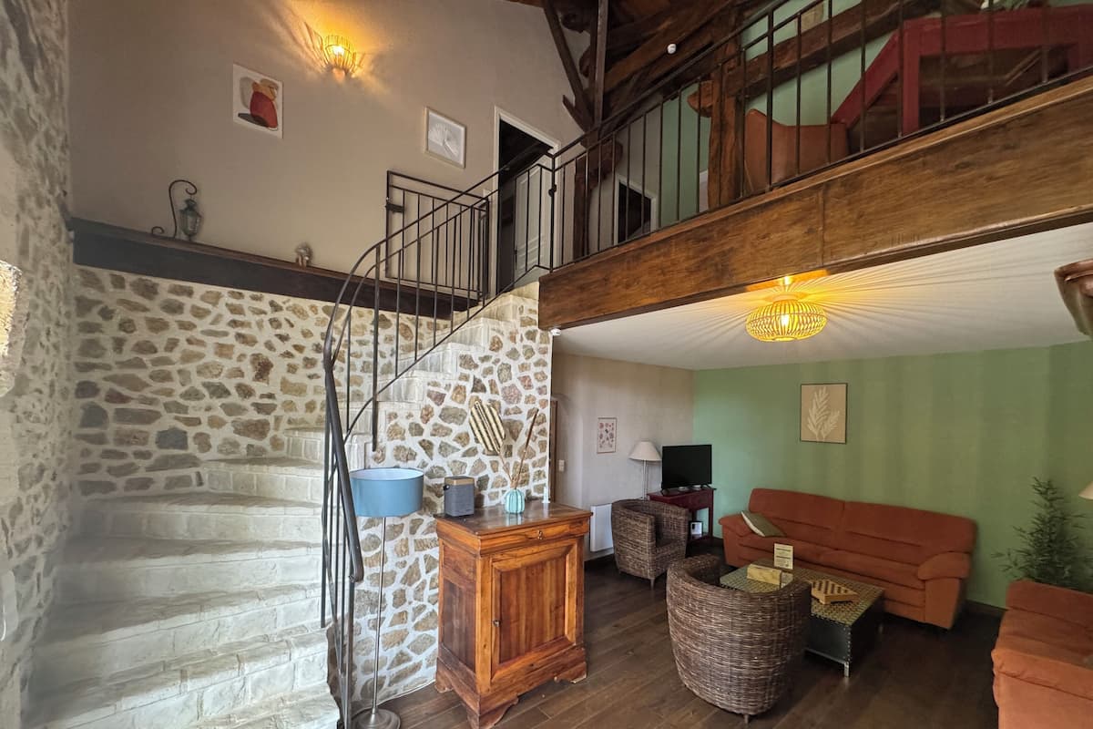 Un intérieur rustique avec un mur en pierre, un escalier en bois, des meubles en osier et un canapé rouge.