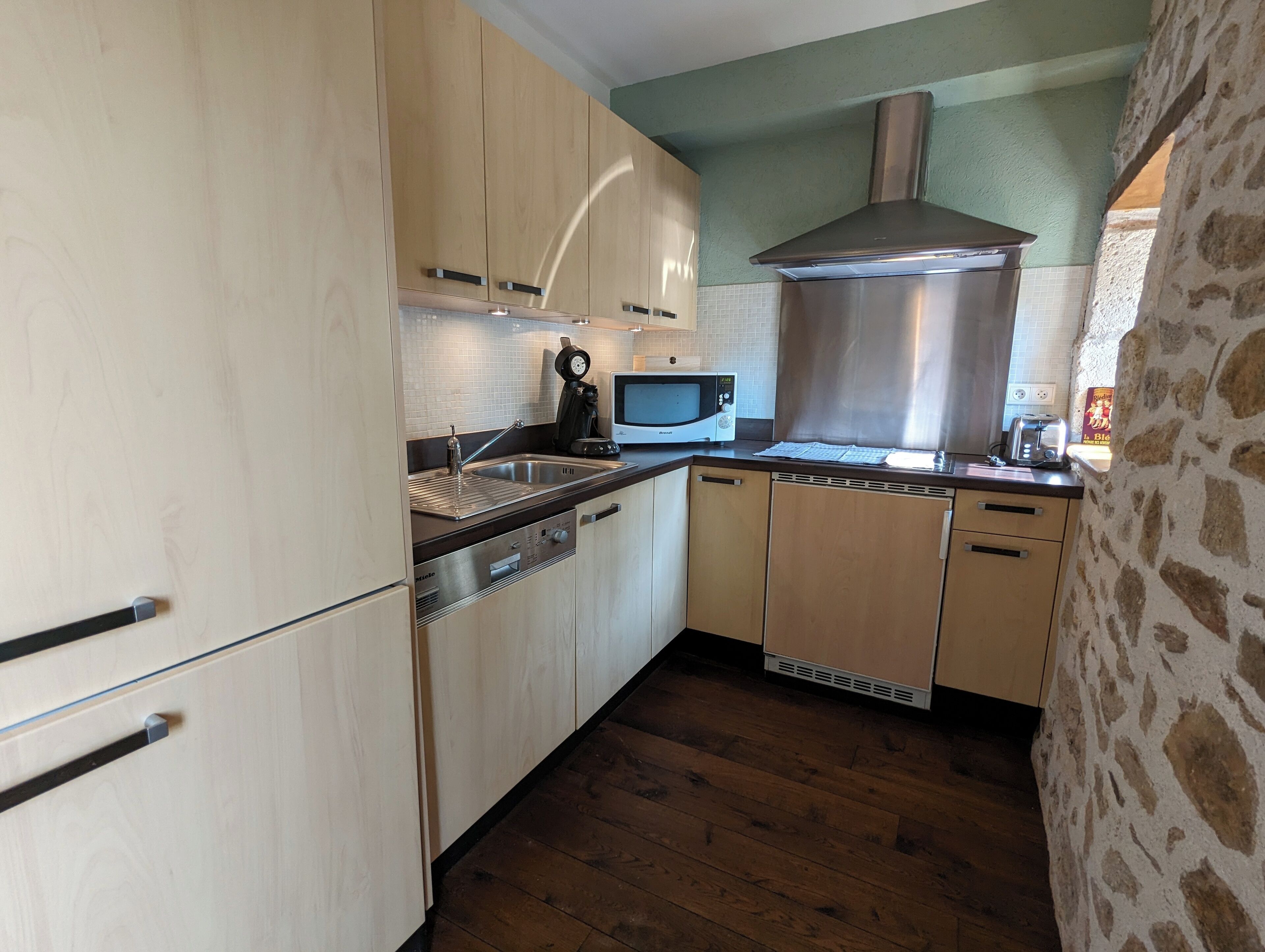 Eine kompakte Küche mit Holzausstattung, einer Edelstahl-Dunstabzugshaube, einer Mikrowelle und einem Toaster.