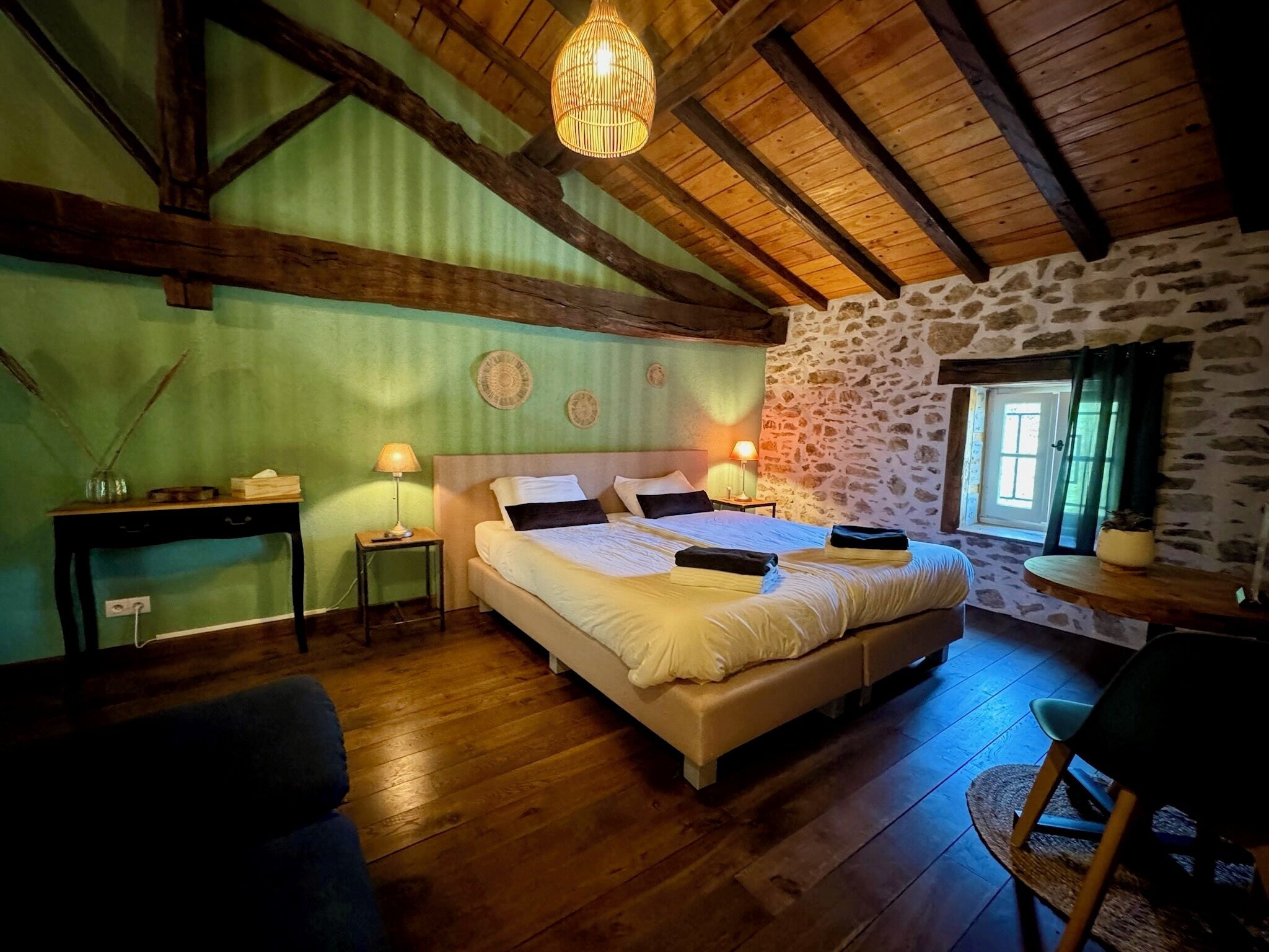 Un dormitorio con una cama grande, vigas de madera, pared de piedra y una lámpara colgante.