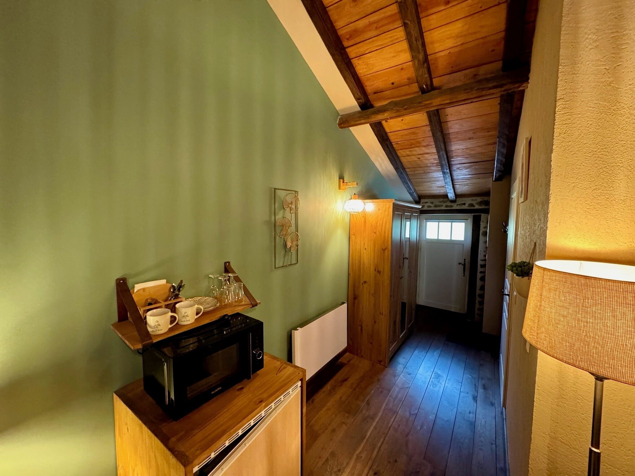 Un pasillo estrecho con pisos y paredes de madera, un armario de madera con microondas y una puerta que da a otra habitación.