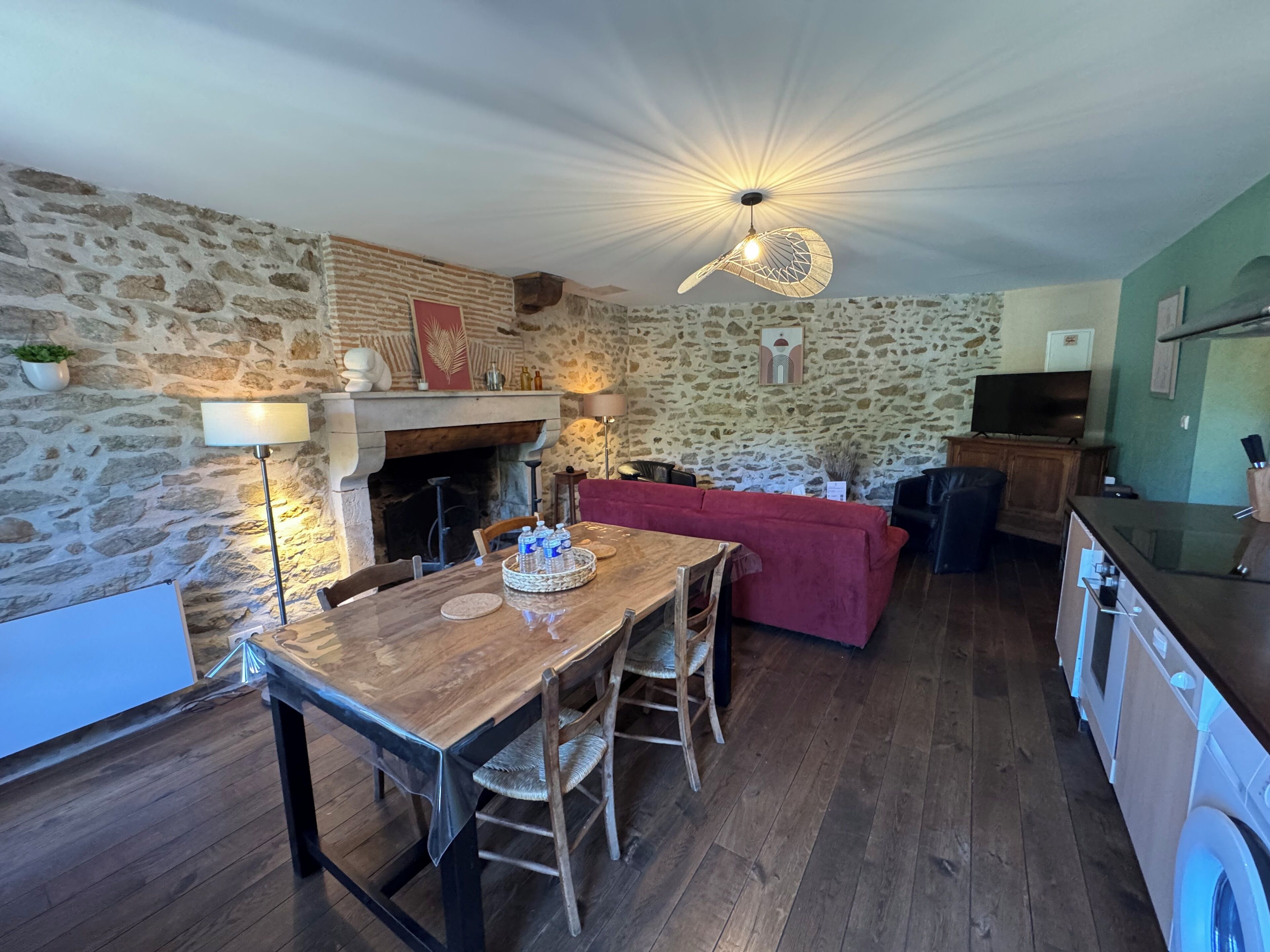 A cozy room with a stone wall, a fireplace, a wooden dining table with chairs, a red sofa, and a television.