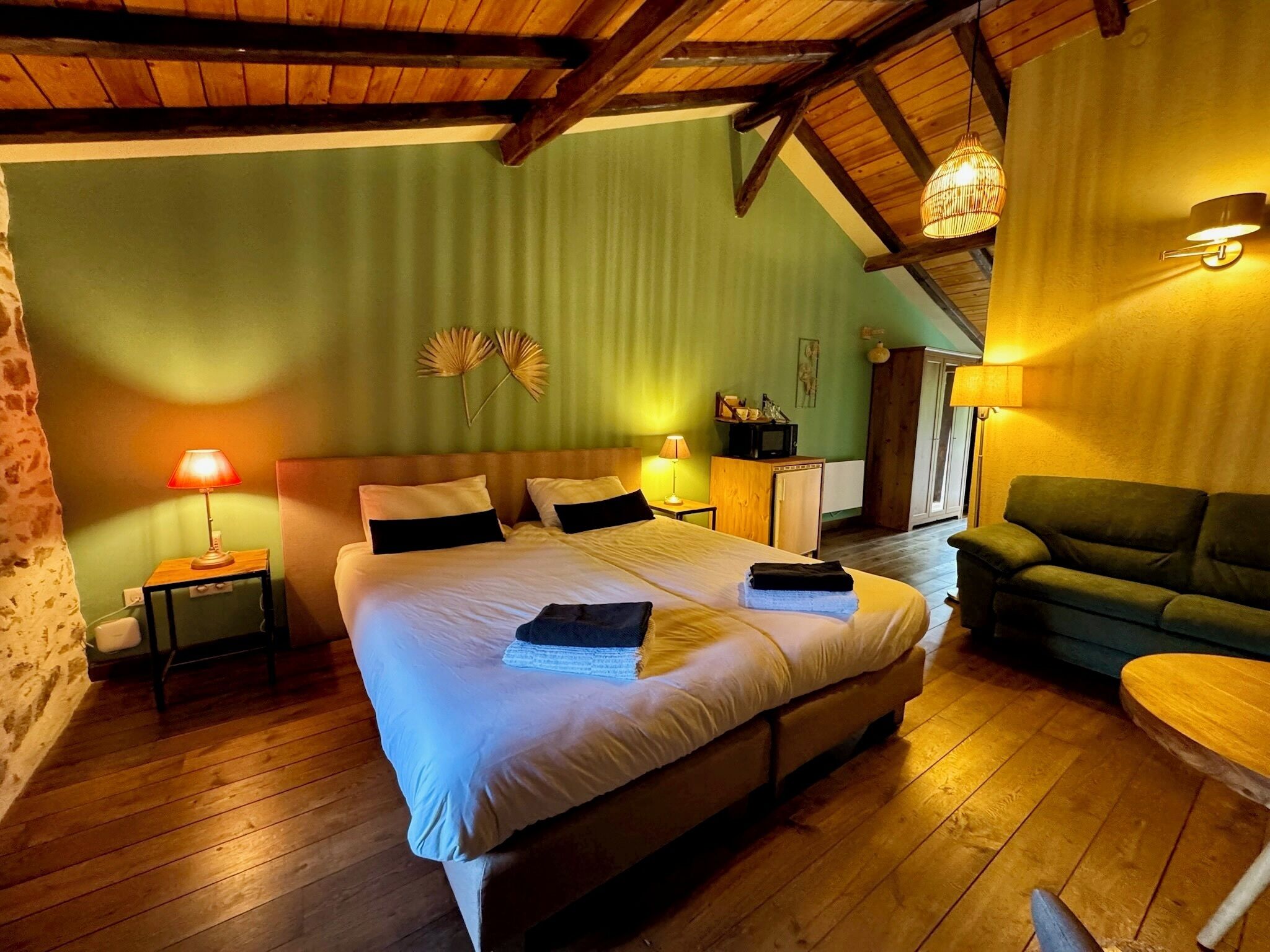 Ein gemütliches Schlafzimmer mit einem großen Bett, einer Holzbalkendecke, einer grünen Wand und einem kleinen Tisch mit einer Lampe.