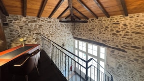Un interior rústico con pared de piedra, vigas de madera en el techo, un escritorio de madera y una escalera.