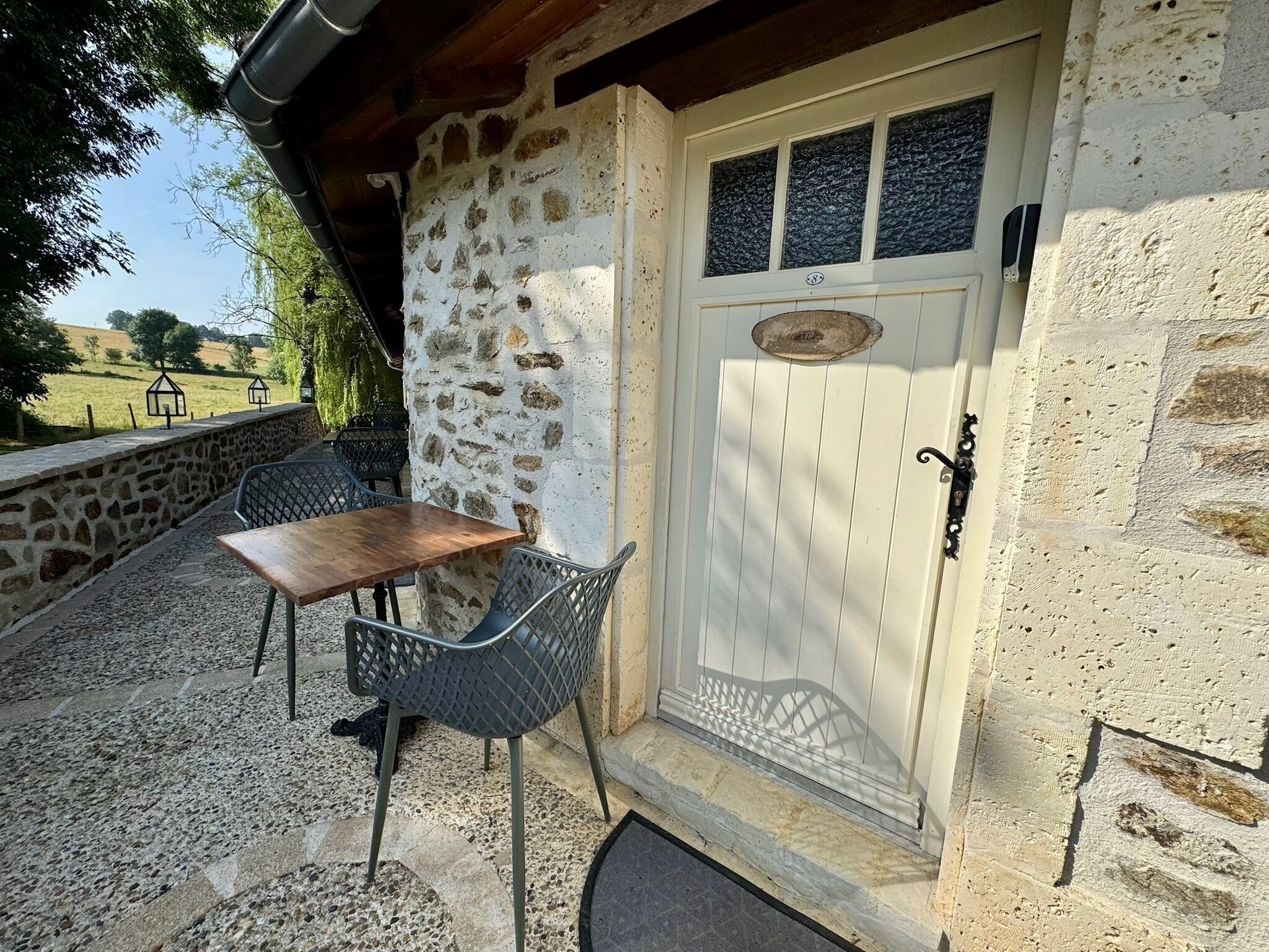 A stone building with a wooden door, a small table, and two chairs outside.