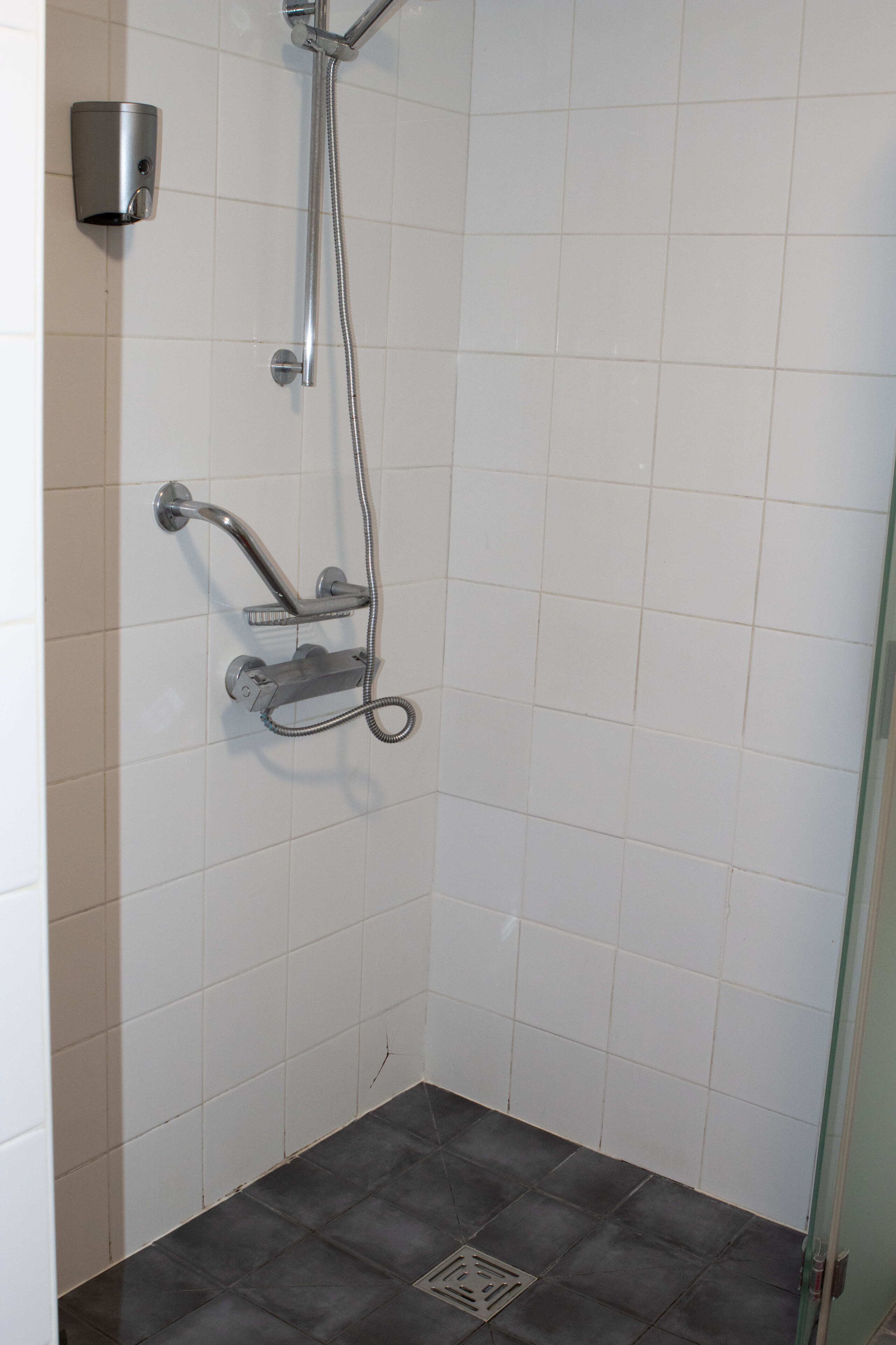 A small, tiled shower area with a handheld showerhead and a wall-mounted faucet.
