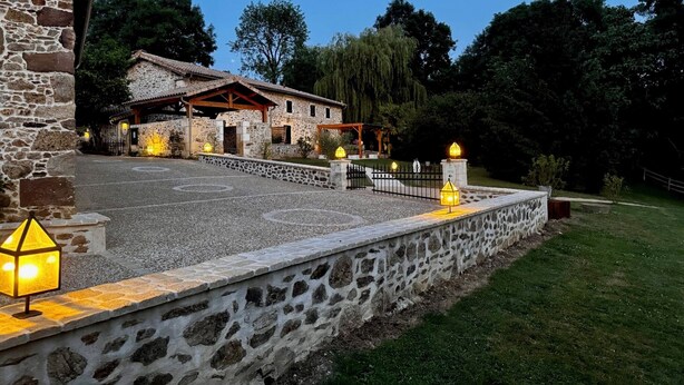 Un edificio de piedra con tejado de tejas, un patio empedrado y una pared de piedra con una linterna.