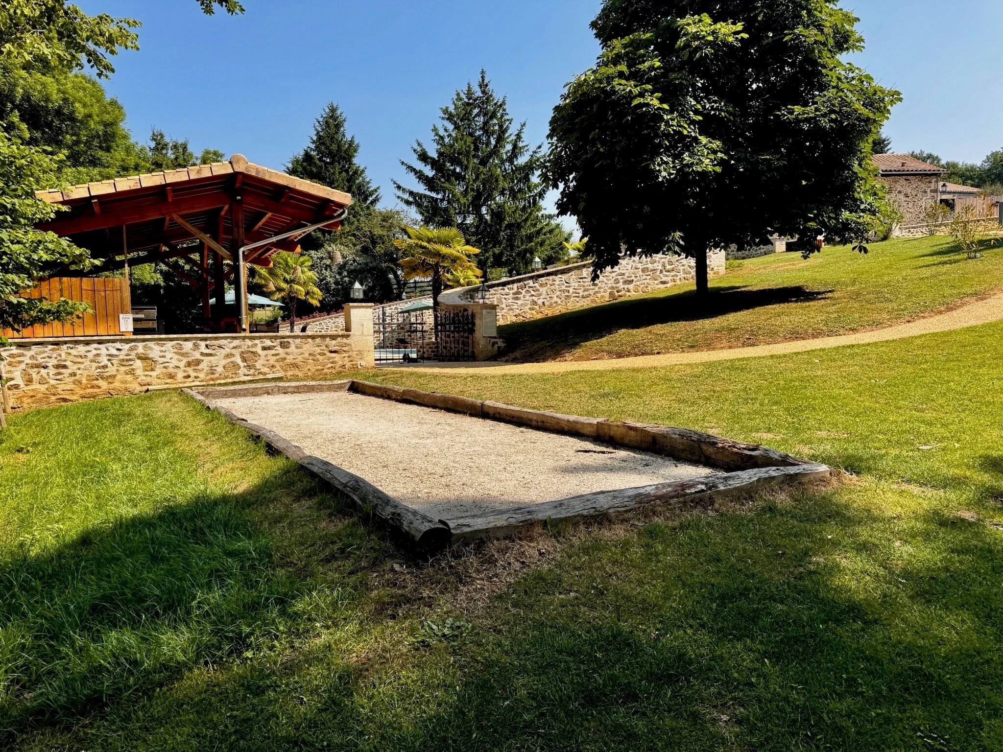 A park with a wooden pavilion, stone walls, and a grassy area with a concrete play structure.