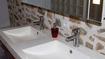 Une salle de bain avec deux lavabos blancs, un distributeur de savon rouge et un miroir au-dessus.