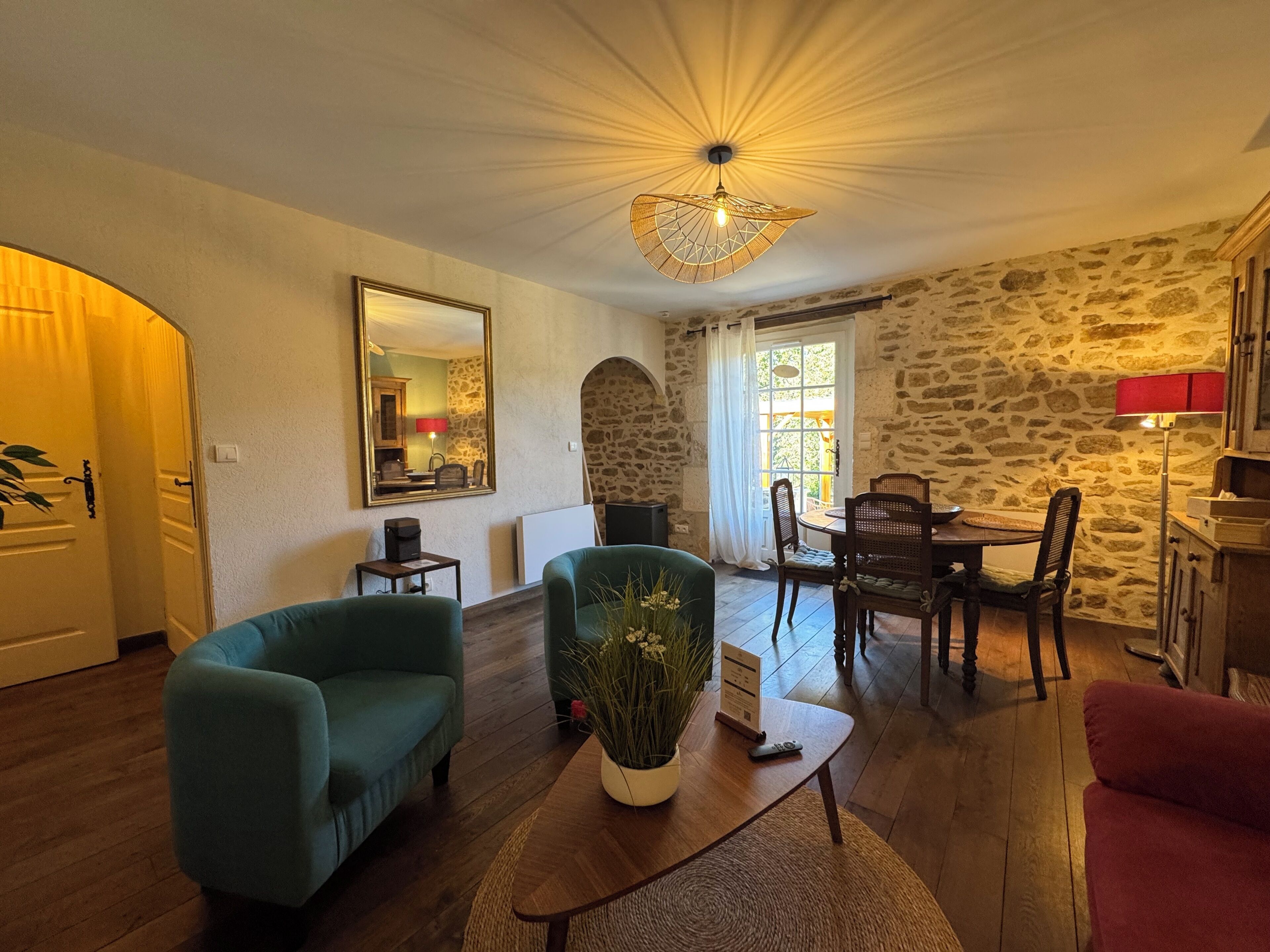 Un salon chaleureux avec un mur en pierre, un coin repas avec une table et des chaises, et un grand miroir accroché au mur.