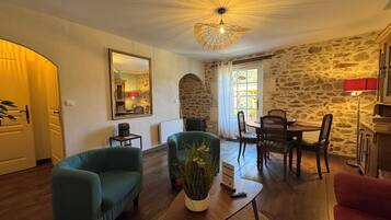 Un salon chaleureux avec un mur en pierre, un coin repas avec une table et des chaises, et un grand miroir accroché au mur.