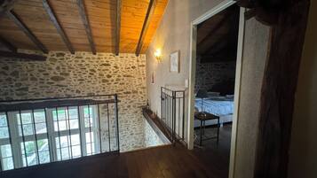 A rustic room with stone walls, wooden beams, a bed, and a staircase leading to an upper level.