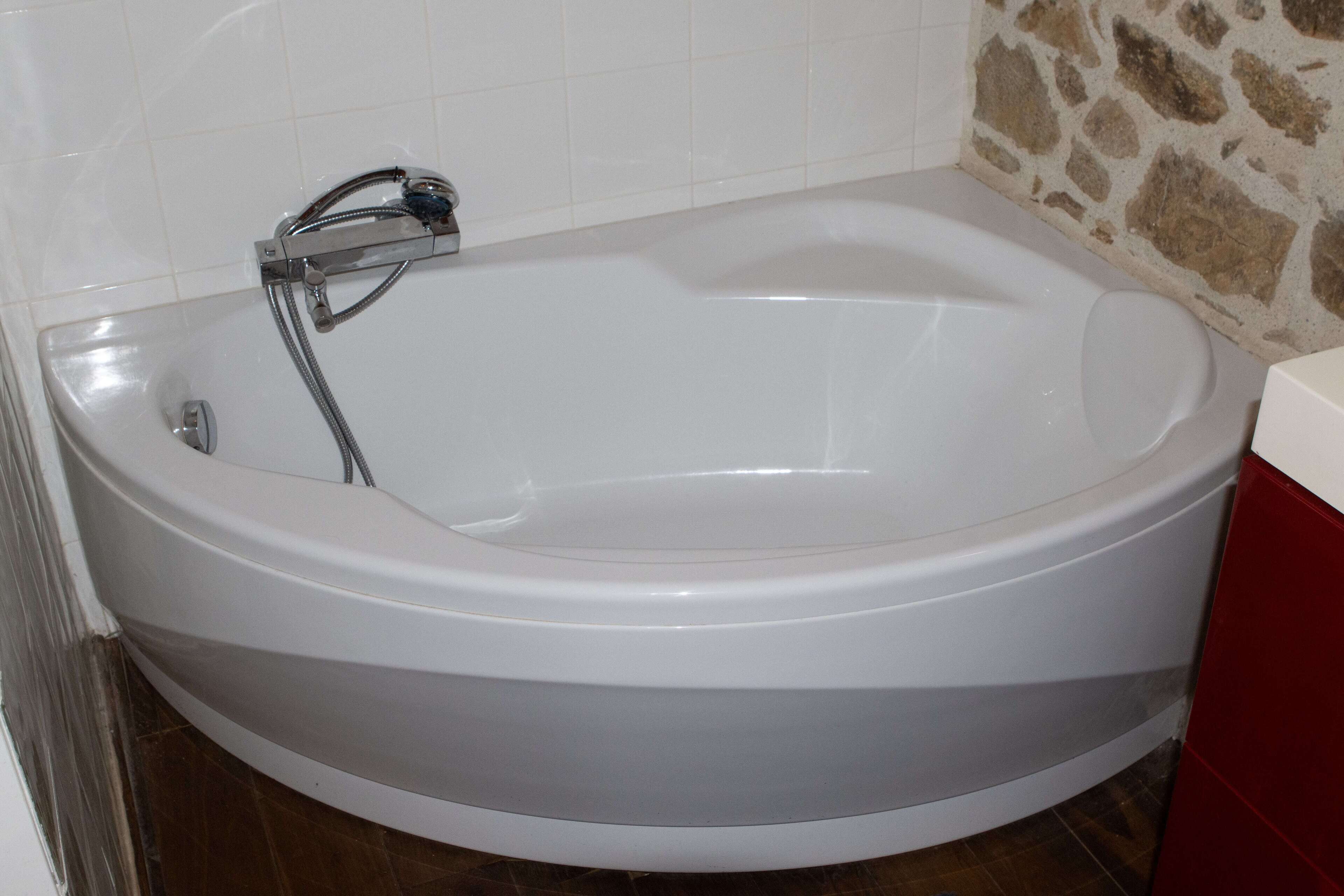 A large, round bathtub with a chrome faucet and showerhead, set against a stone wall and white tiled background.