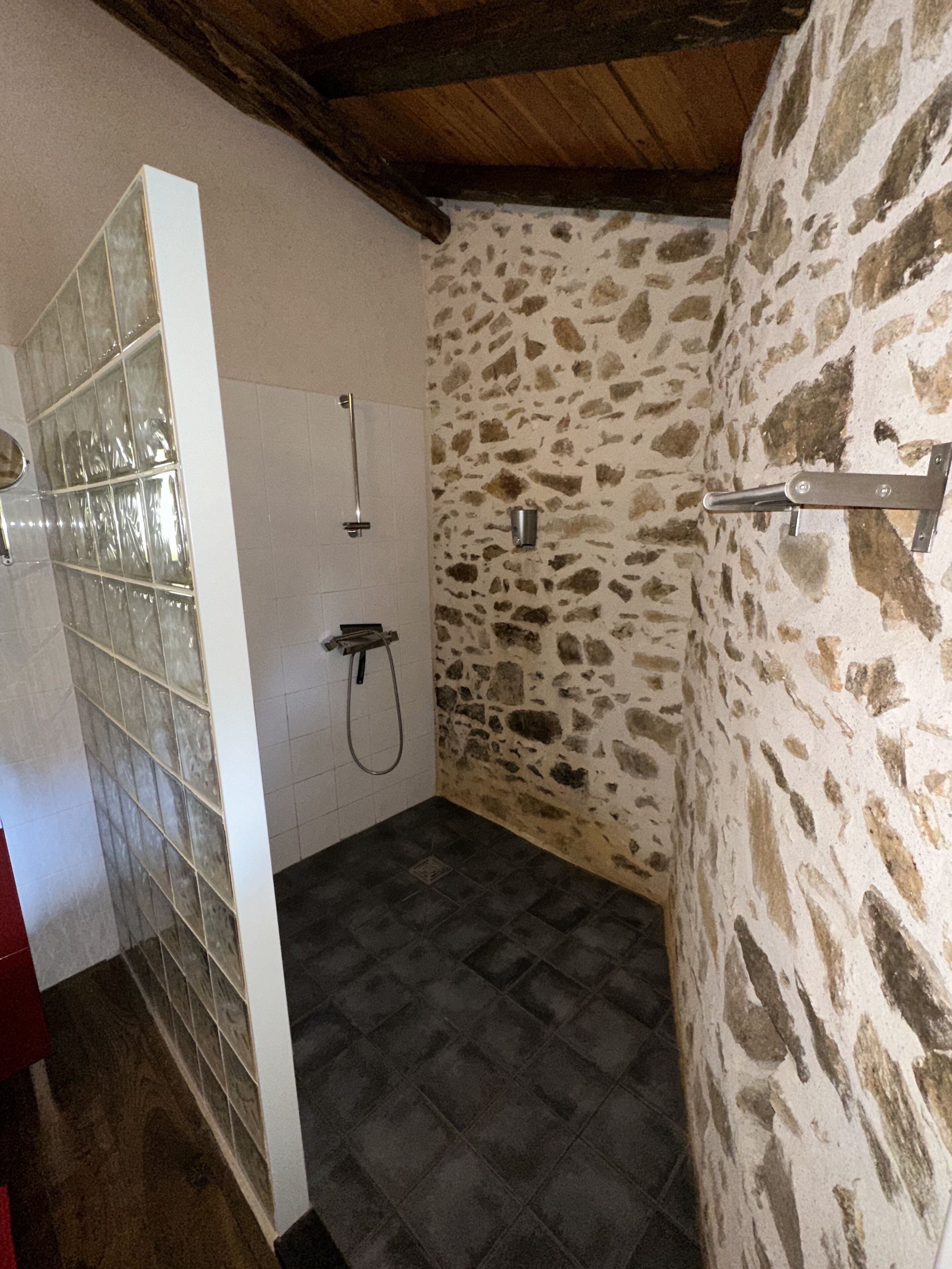 Une salle de bain avec un mur en pierre, une douche et un sol carrelé.