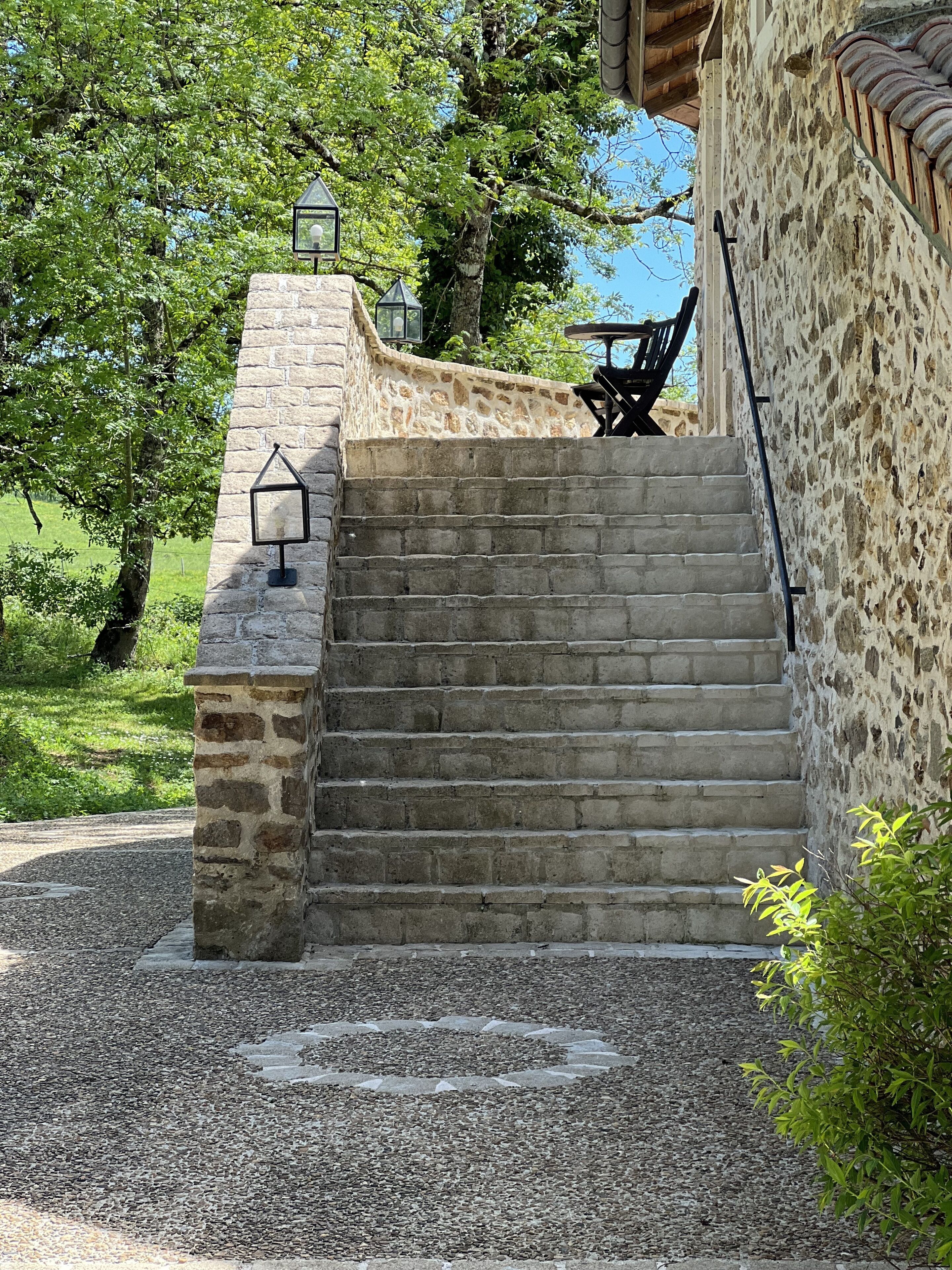 Un escalier en pierre mène à un espace extérieur abrité, aménagé avec une table et des chaises.