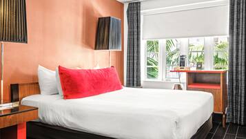 A hotel room with a large bed, a desk with a coffee machine, and a view of greenery outside.