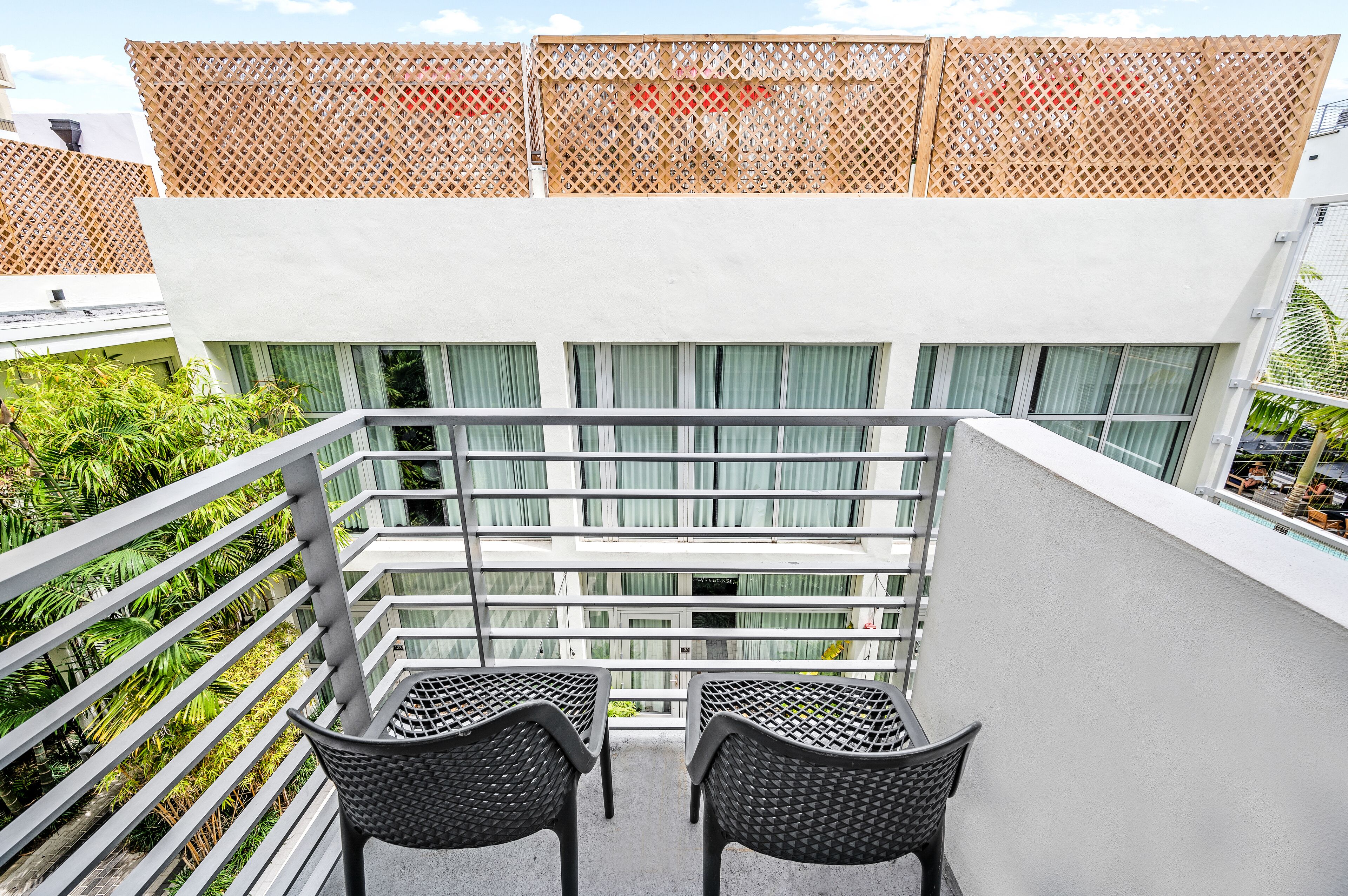 A balcony with two chairs, a white railing, and a view of a building with multiple windows.