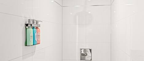 Une salle de bain moderne avec des carreaux blancs, une pomme de douche et trois bouteilles de savon BION.