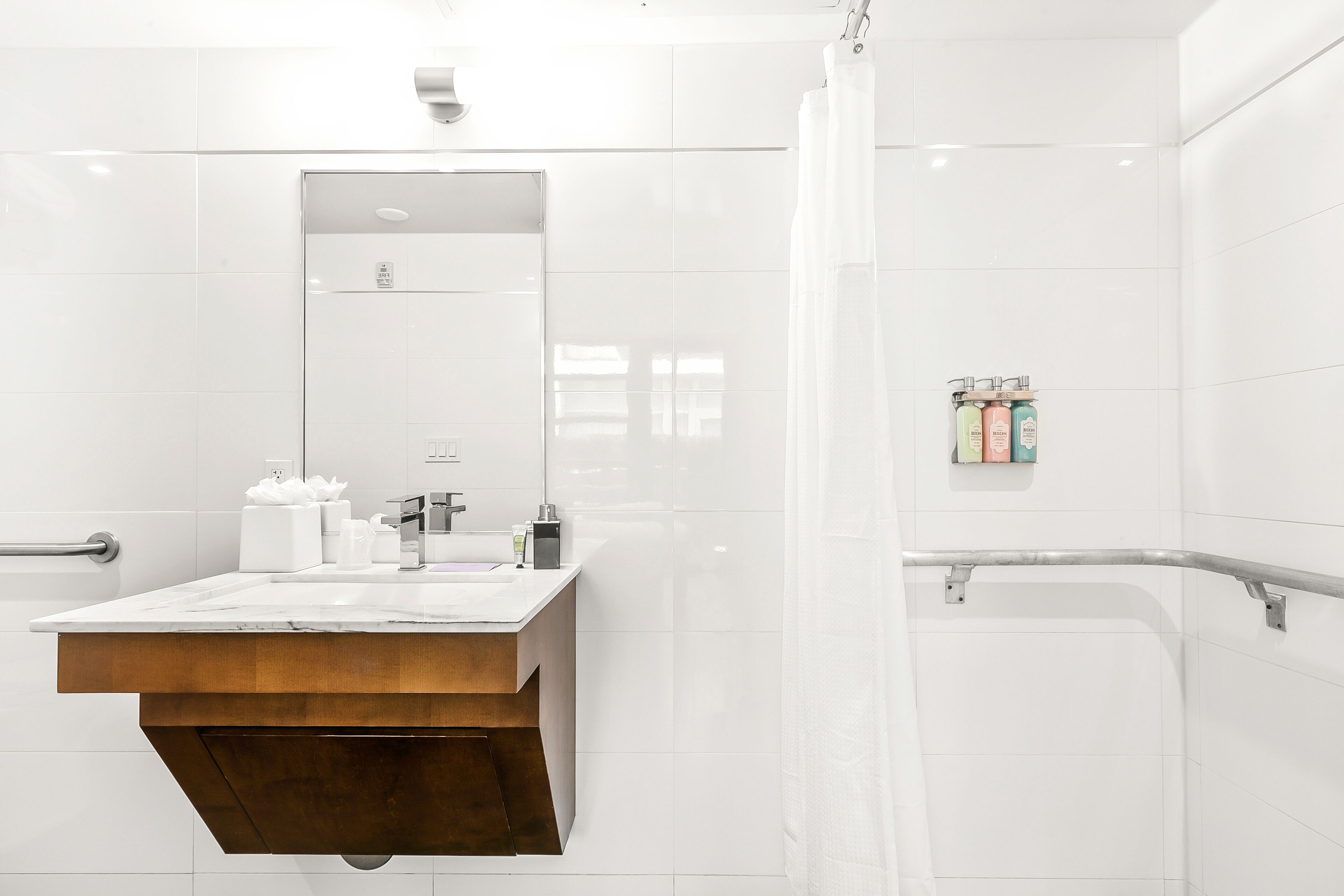 Ein modernes Badezimmer mit einem großen Spiegel, einem Holzwaschtisch, einer Dusche mit Glastür und einer Haltestange.