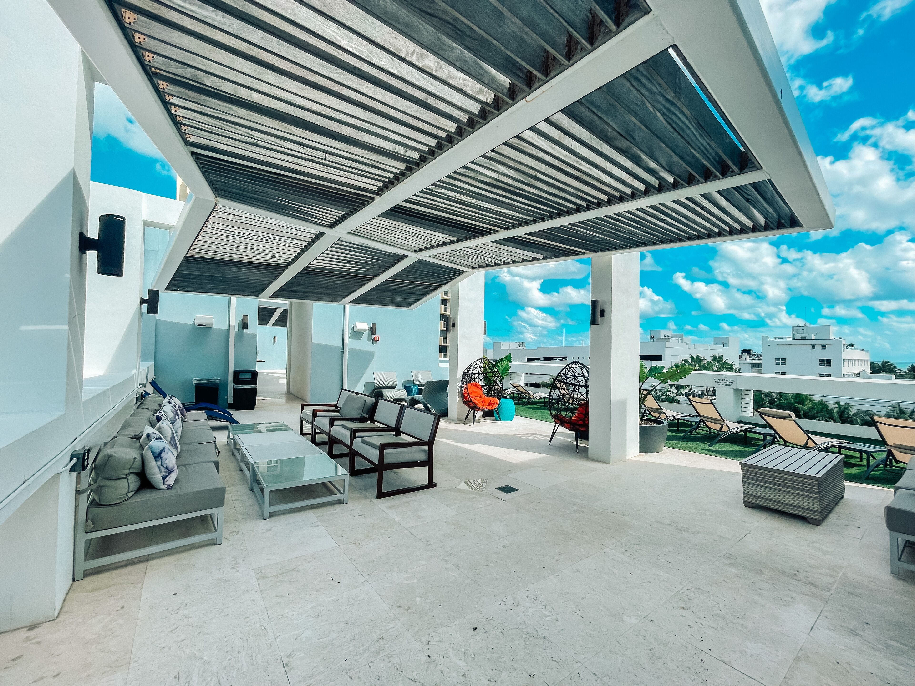 A modern outdoor lounge area with a covered patio, seating arrangements, and a view of the cityscape.