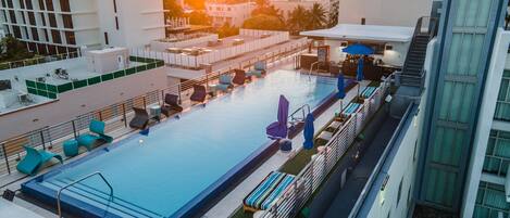 A rooftop pool with lounge chairs and umbrellas, surrounded by modern buildings.