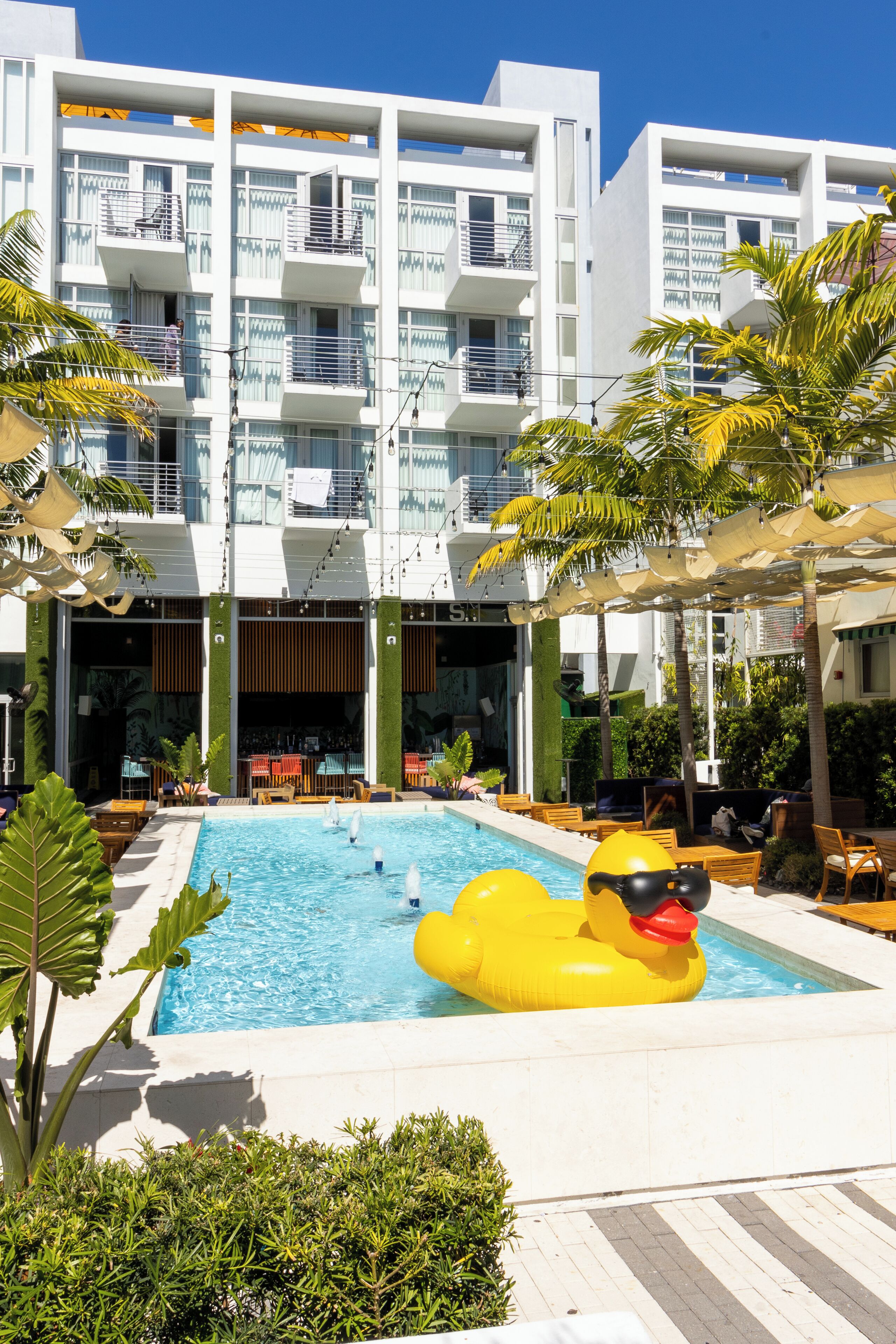 A modern hotel with a swimming pool, outdoor seating, and balconies.