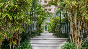 A pathway flanked by bamboo and tropical plants leading to a building with balconies. - The Fairwind Hotel (Miami Beach)