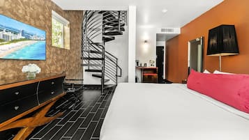 A modern hotel room with a large bed, a TV on the wall, a wooden dresser, and a spiral staircase.