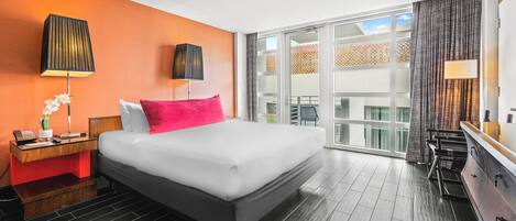 Habitación de hotel con una cama grande, una mesita de noche con lámpara, cómoda y vistas al exterior a través de un amplio ventanal.