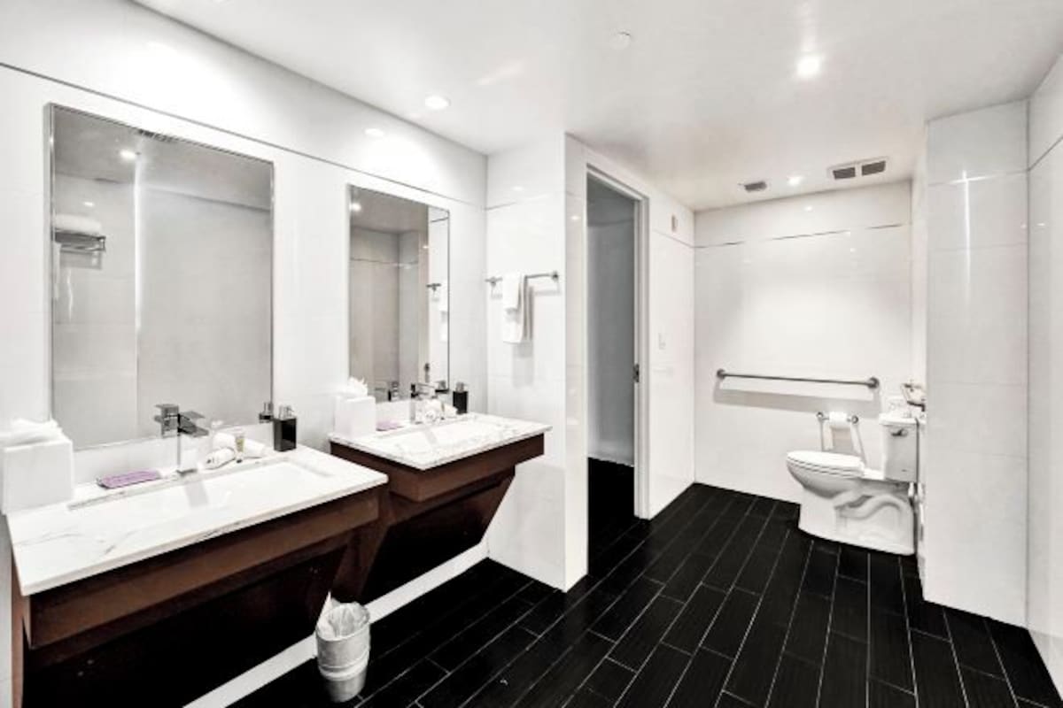 A modern bathroom with two sinks, a large mirror, a toilet, and a black tiled floor.