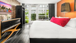 A hotel room with a large bed, a TV on the wall, a desk with a computer, and a view of the outside balcony. - The Fairwind Hotel (Miami Beach)