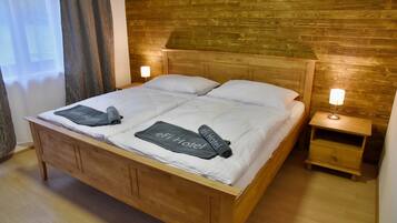 Una cama de madera con dos almohadas y una colcha, una mesita de noche con una lámpara, y un cabecero de madera.