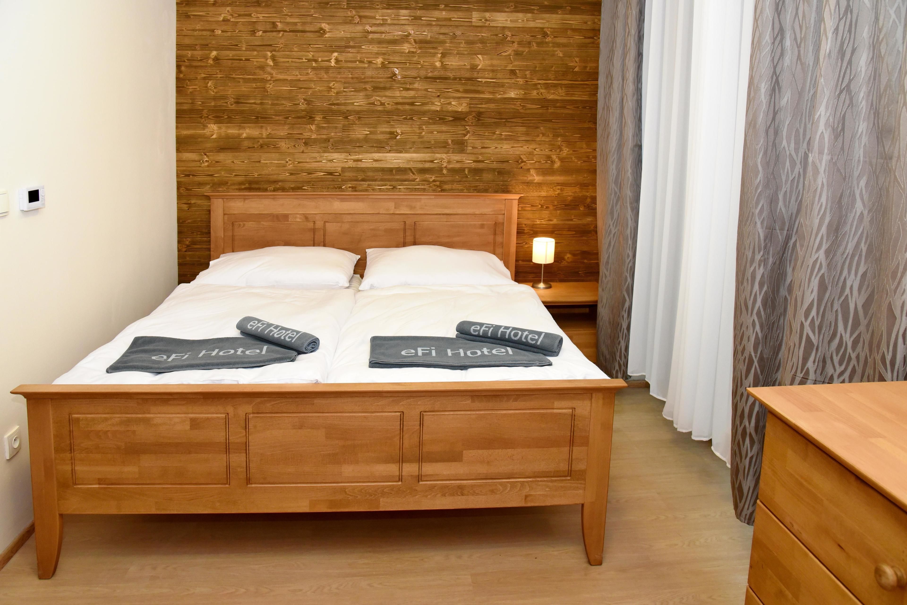 A wooden bed with two pillows and a blanket, a nightstand with a lamp, and a wooden dresser.