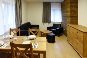 Un comedor con una mesa de madera dispuesta para dos personas, dos sofás negros, un mueble de madera y un reposapiés negro.
