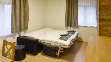 A small, compact room with a single bed, a wooden table, a chair, and a suitcase.