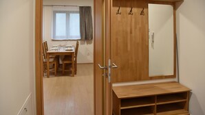 Ein Zimmer mit einem Holzschrank, einem Esstisch mit Stühlen und einem Fenster mit Vorhängen.