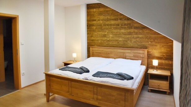 Ein Schlafzimmer mit einem hölzernen Bett, zwei Nachttischen mit Lampen und einer schrägen Decke mit Holzverkleidung.