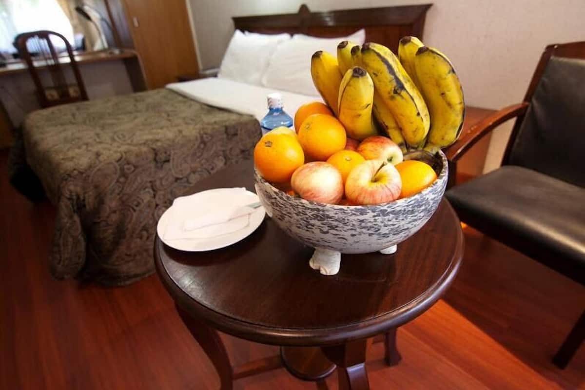 A hotel room with a bed, a dining table with a fruit bowl, and a chair.