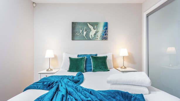 A neatly made bed with a blue blanket, two green pillows, and two bedside lamps on white nightstands. - Elliot Suite No2 - Donnini Apartments (Ayr)