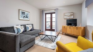 A living room with a grey sofa, a yellow armchair, a wooden coffee table, a TV on a wooden cabinet, and a framed picture on the wall. - Elliot Suite No2 - Donnini Apartments (Ayr)