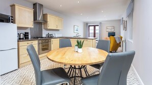 A modern kitchen with wooden cabinets, a stainless steel range hood, and a round dining table with four chairs. - Elliot Suite No2 - Donnini Apartments (Ayr)