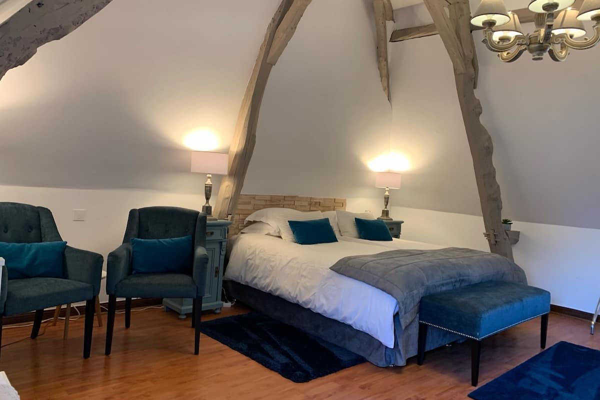 A bedroom with a large bed, two chairs, a nightstand, and a chandelier.