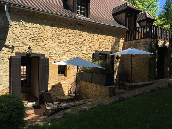 A stone building with a balcony, outdoor seating, and a door leading to an interior space. - Le Noyer Résidence (Le Bugue)