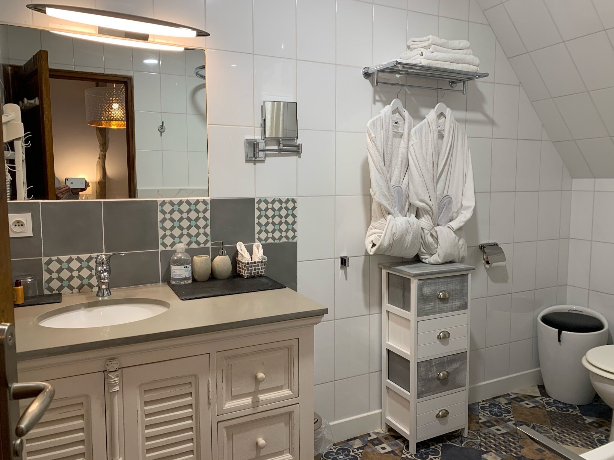 Een moderne badkamer met een grote spiegel, witte tegels, een wastafel met kastje en een toilet.