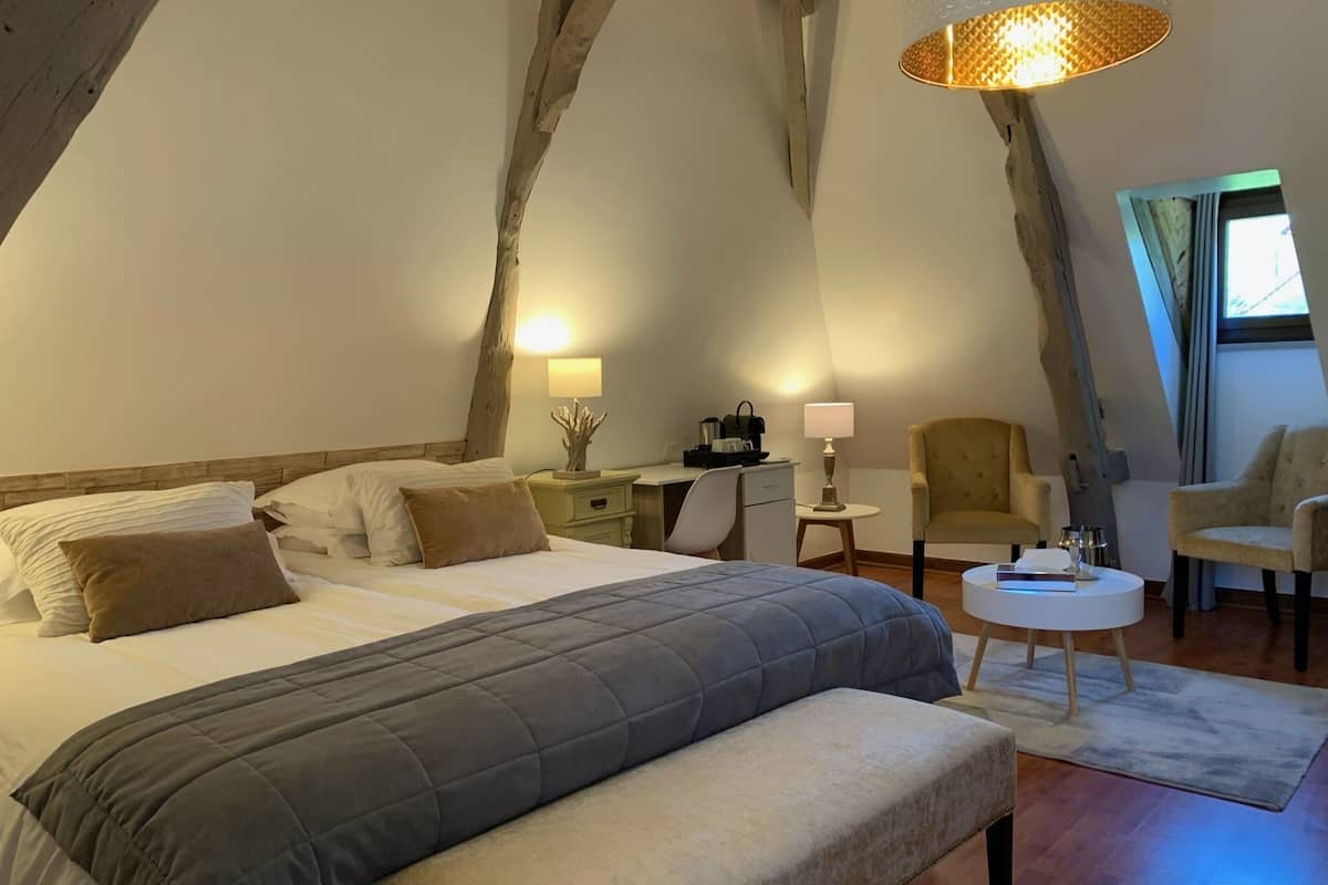 A bedroom with a large bed, a desk, two chairs, and a small round table.