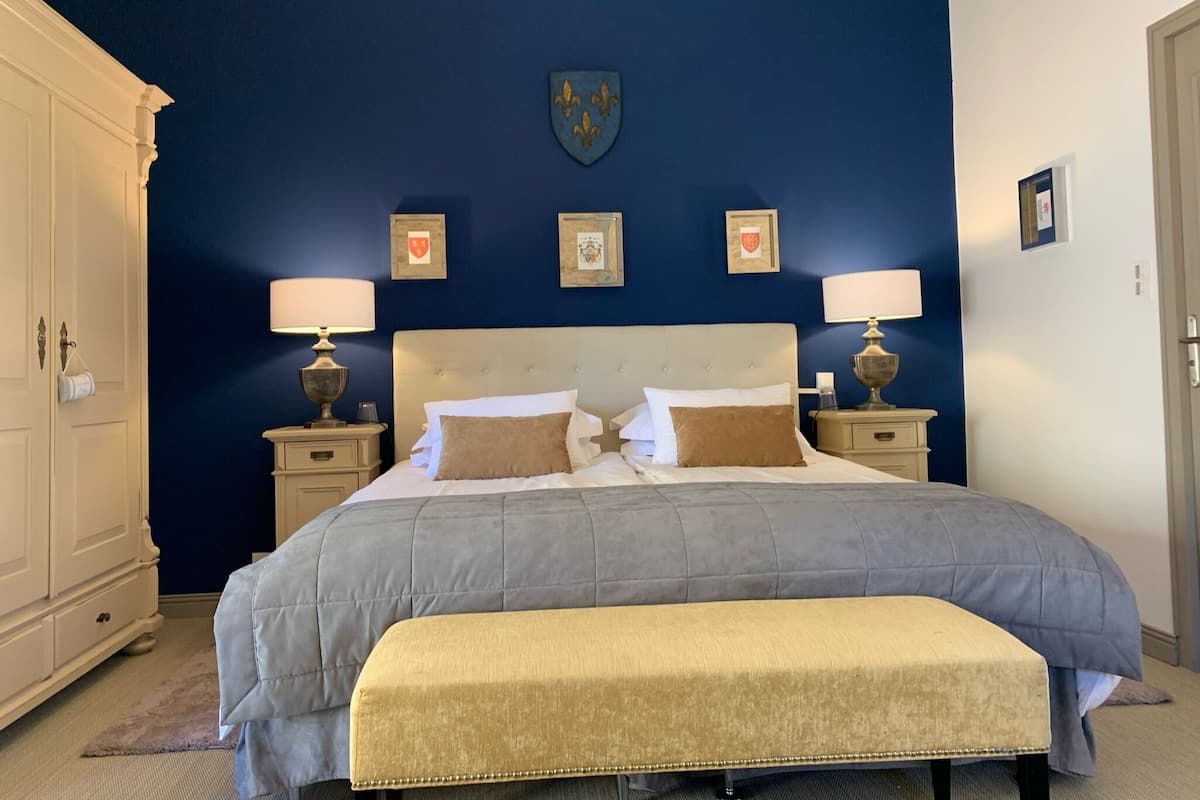 A bedroom with a large bed, two bedside tables, a bench, and a wardrobe.
