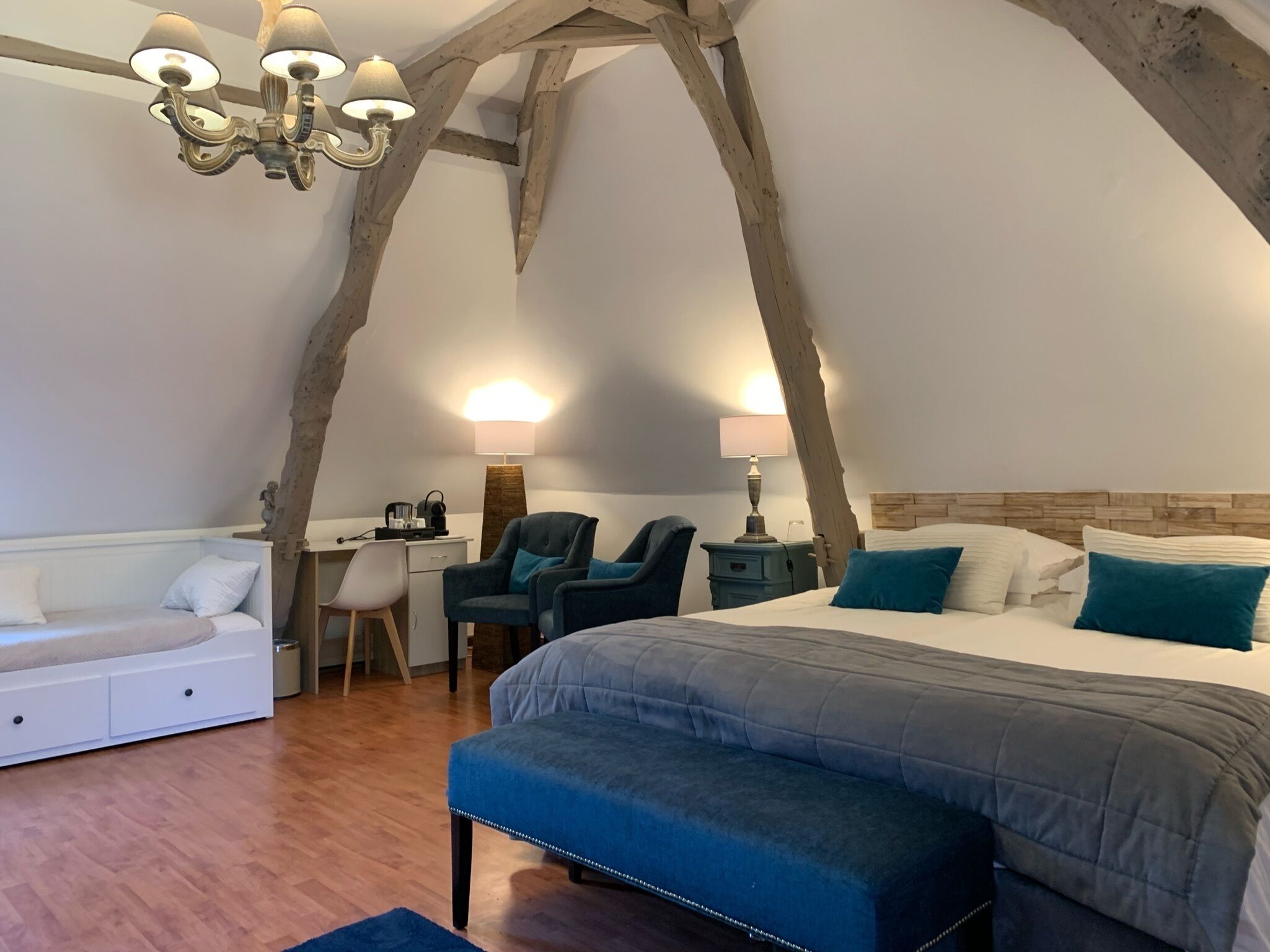 Une chambre à coucher avec un grand lit, un bureau, deux chaises, un canapé et un lustre.