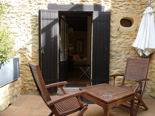 A stone building with a wooden door, two wooden chairs, and a table with a glass.